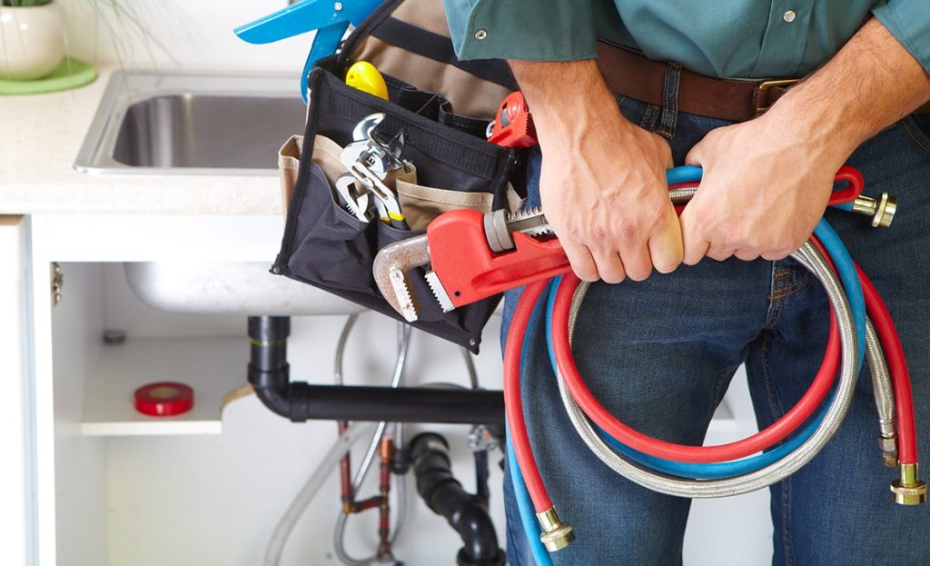 Plumber In Front Of Sink Holding Wrench And Pipes