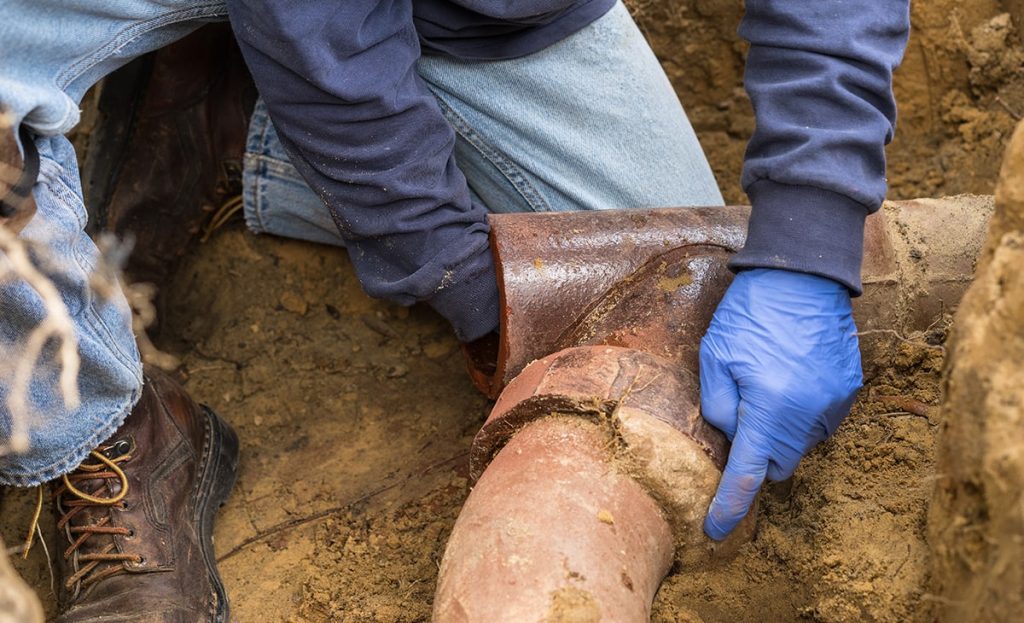 Plumber Pointing At Rusted Sewer Pipes Underground